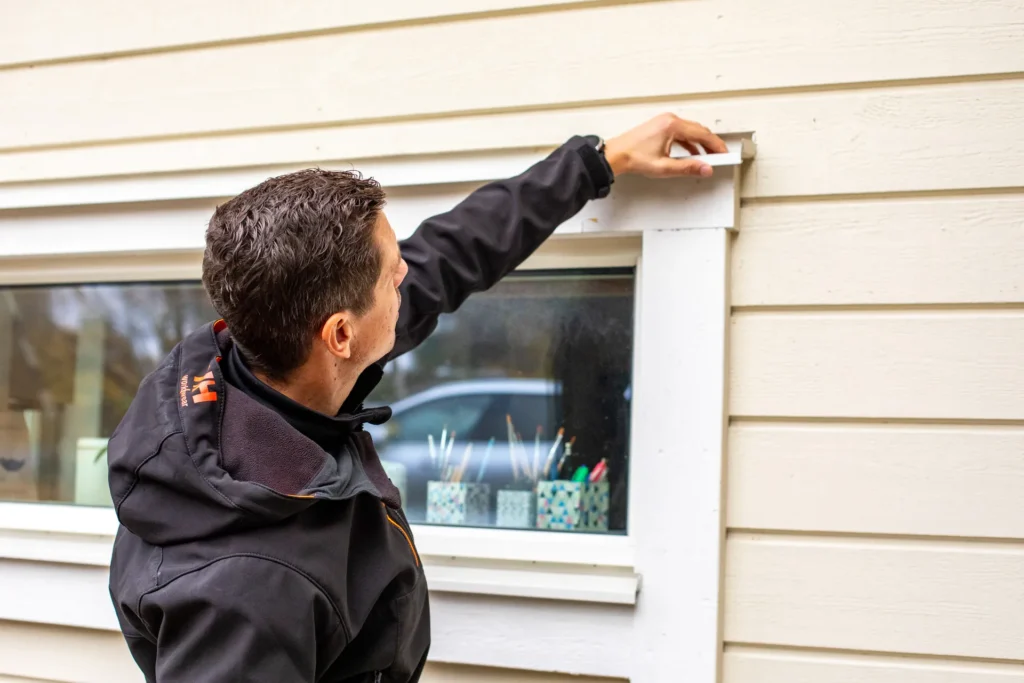 Besiktningsman kontrollerar plåtarbete runt fönster vid överlåtelsebesiktning.